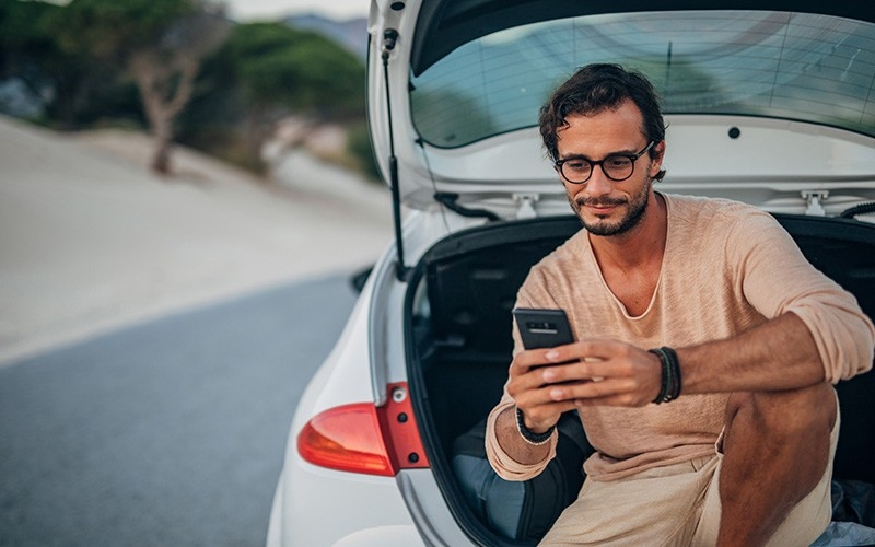 Chico usando la app Waylet sentado en el maletero de su coche